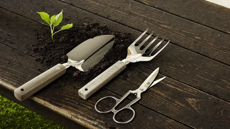 Planteske, havesaks og håndgaffel på et vejrbidt havebord med jord og blade